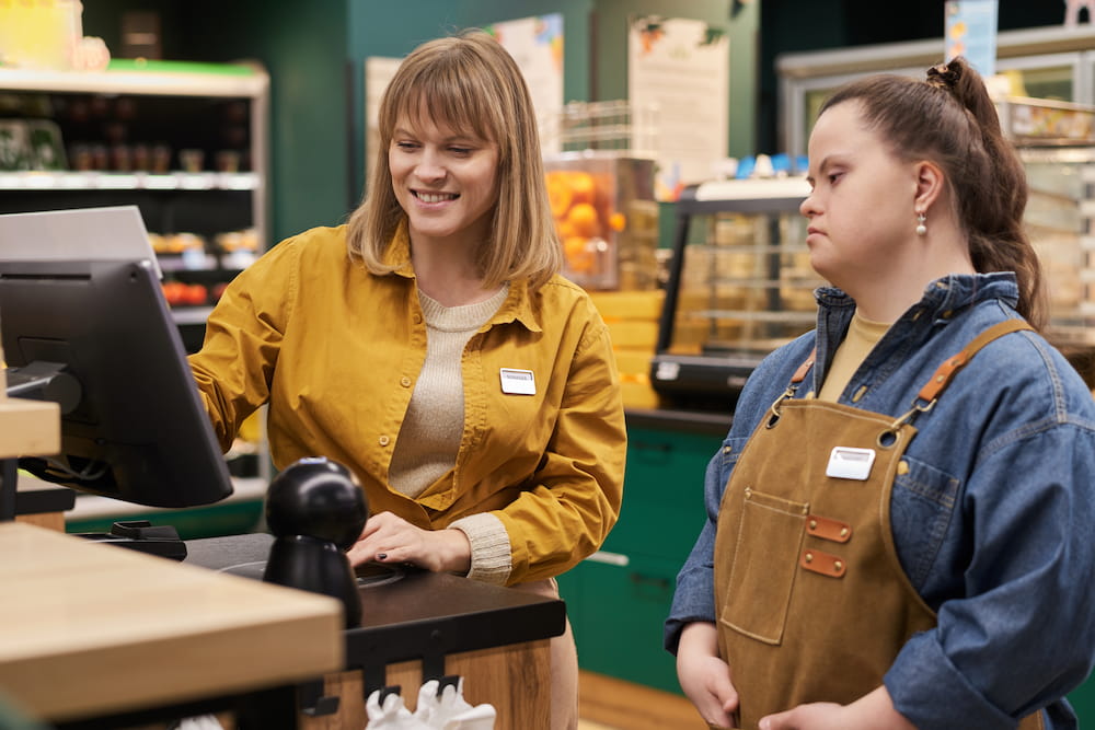 NJ DDD Services job coach trains a woman with Down syndrome to use a grocery store cash register.