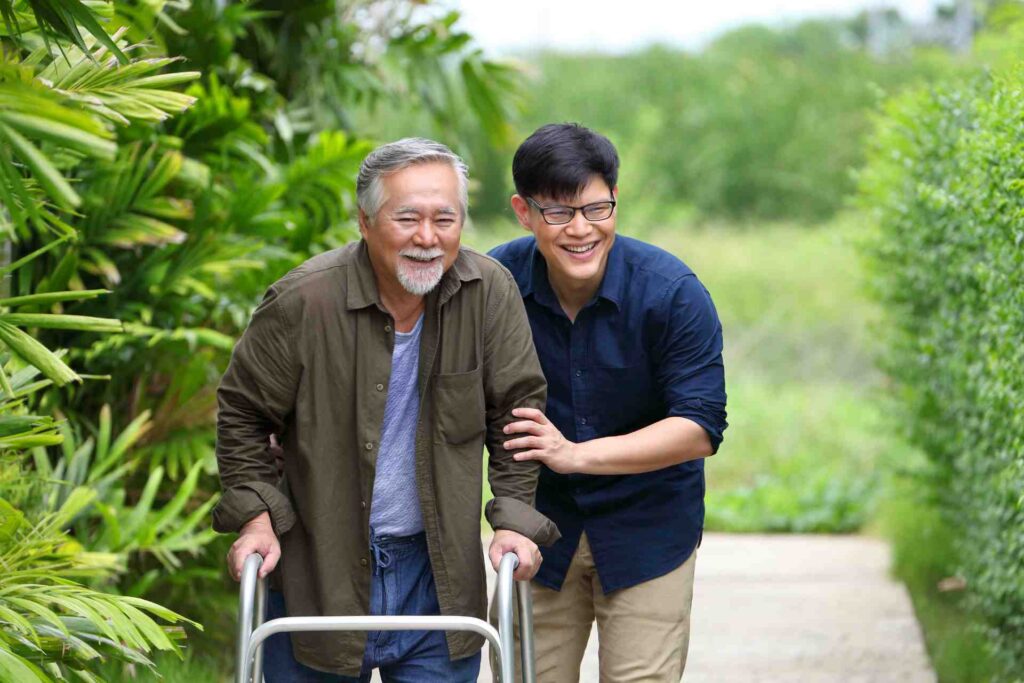 Caregiver helping an older adult walk outdoors with a walker
